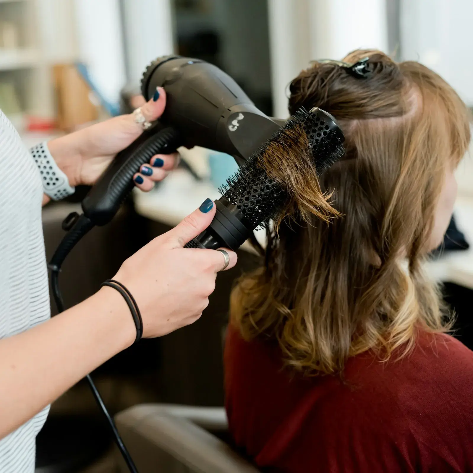 Coiffeur föhnt die Haare einer Kundin
